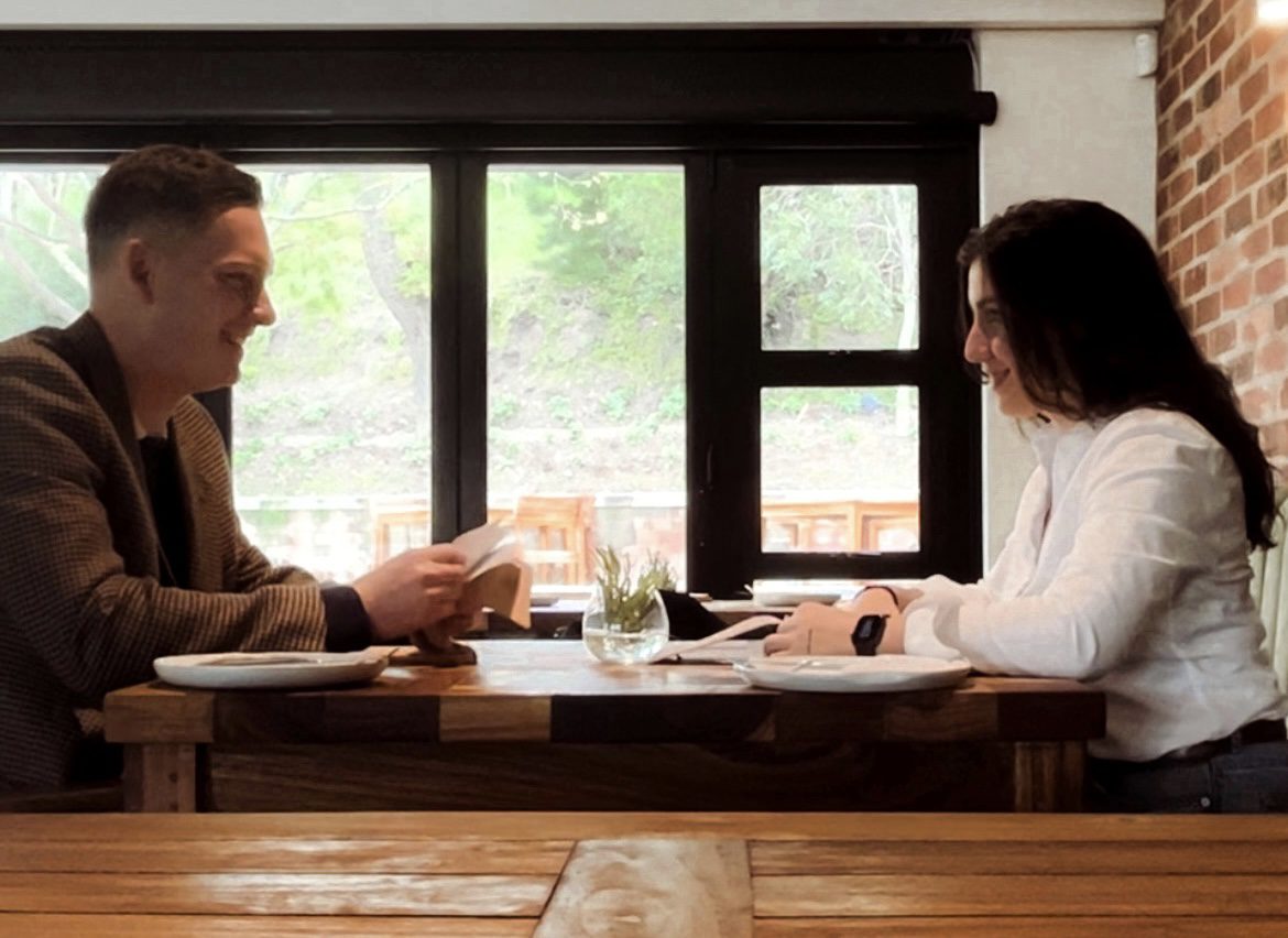 Jessica and Greg, seated at a charming table at Pink Valley Wine Farm, eagerly perusing the menu and sharing smiles as they prepare to order a delightful array of dishes.